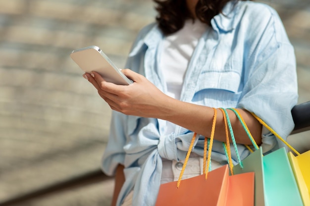 Una giovane donna europea con molte borse della spesa in mano si diverte a fare acquisti online sul telefono cellulare