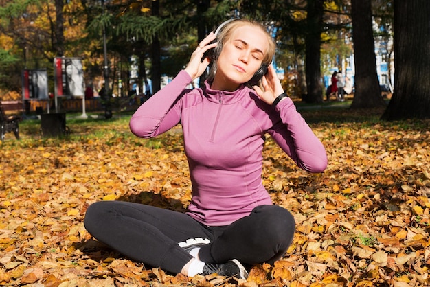 Una giovane donna fa sport all'aperto in un parco autunnale e ascolta musica con le cuffie