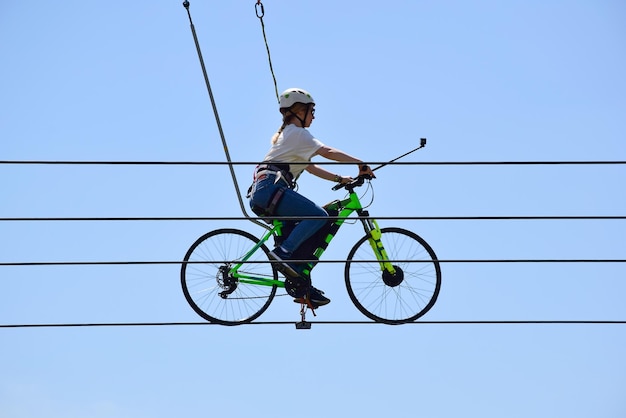 Una giovane donna fa un giro in bicicletta su corde sopra il suolo sullo sfondo del cielo