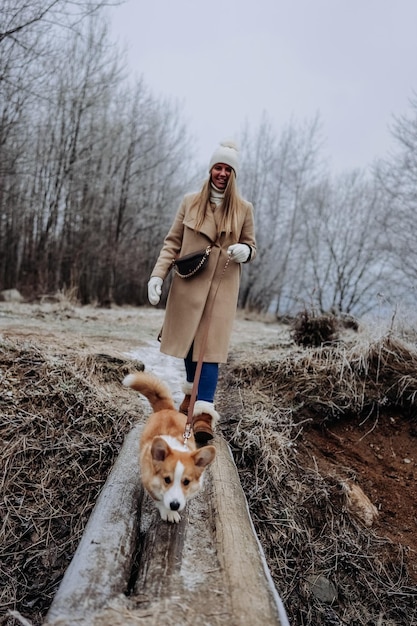 Una giovane donna felice che cammina con il suo cucciolo di Welsh Corgi Pembroke natura invernale