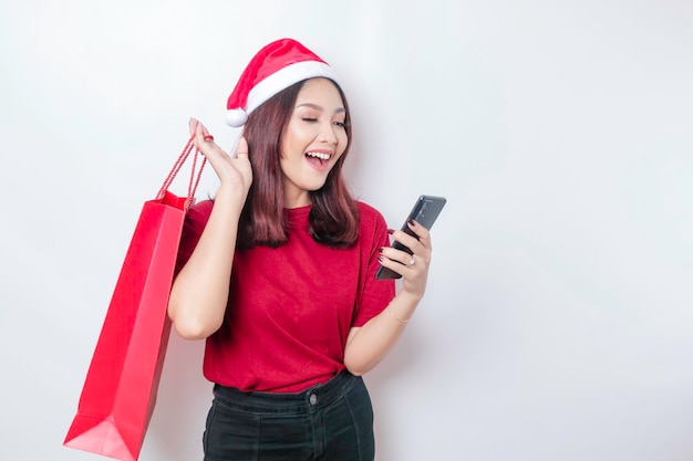 Una giovane donna felice che indossa il cappello di Babbo Natale 39 sorride mentre tiene in mano i regali di Natale e il suo smartphone