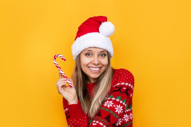 Una giovane donna felice con un caldo maglione di cervo rosso e un cappello di Babbo Natale con un bastoncino di zucchero a strisce in mano