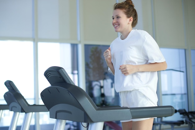 Una giovane donna felice e in forma che si allena in palestra, che corre, che corre sul tapis roulant, che fa esercizi cardio e...