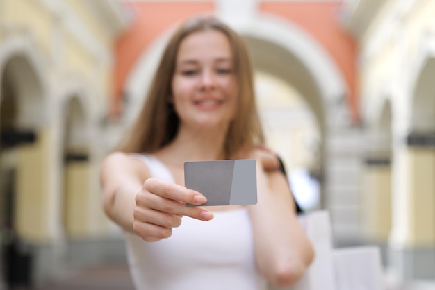 Una giovane donna felice e sfocata mostra una carta di credito in mano e sorridendo durante lo shopping