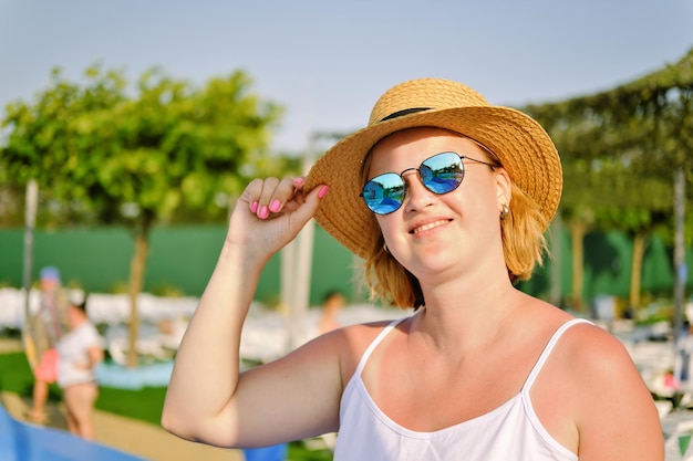 Una giovane donna felice e sorridente con un cappello di paglia e occhiali da sole che si gode le sue vacanze estive.