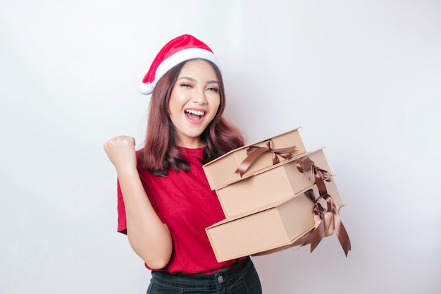 Una giovane donna felice indossa il cappello di Babbo Natale e tiene in mano i regali di Natale