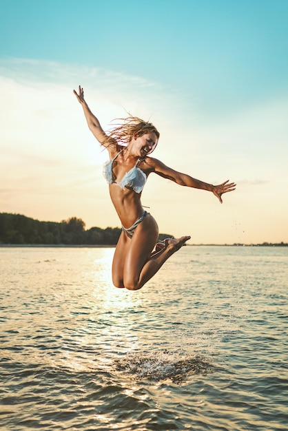 Una giovane donna felice si diverte in spiaggia. Si sta divertendo e saltando sull'acqua.