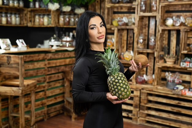 Una giovane donna felice sta tenendo e vendendo frutta fresca in un negozio di alimenti naturali.