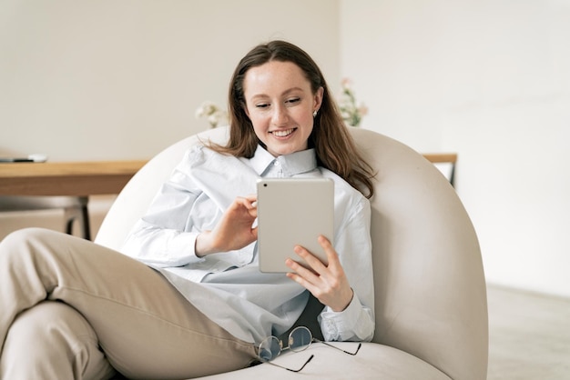 Una giovane donna felice un manager creativo che utilizza un tablet portatile su una comoda sedia a casa