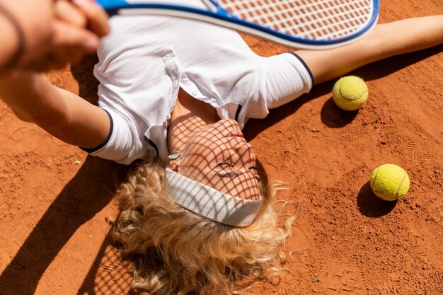 una giovane donna giace sul campo da tennis sull'erba indossando un costume sportivo bianco