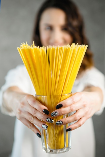 Una giovane donna graziosa con una camicia bianca in cucina con in mano un mazzo di spaghetti di pasta