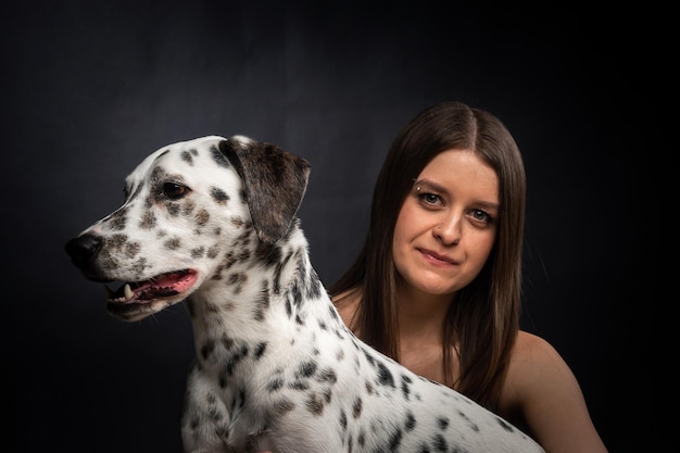 Una giovane donna graziosa sta giocando con il suo animale domestico dalmata isolato su uno sfondo nero Ritratto in studio del cane e del proprietario