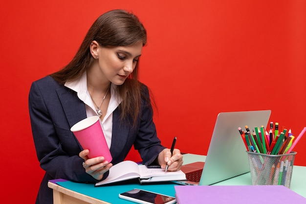 Una giovane donna in abiti d'affari scrive i piani in un diario e beve caffè