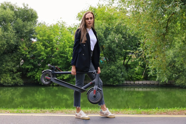 Una giovane donna in abiti eleganti posa con uno scooter elettrico nel parco