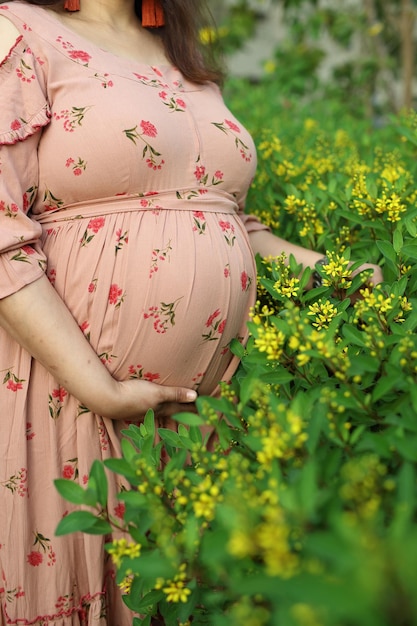 Una giovane donna in abito attillato stampato rosa abbraccia il suo ventre con un futuro bambino.