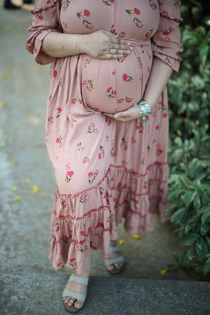 Una giovane donna in abito attillato stampato rosa abbraccia il suo ventre con un futuro bambino.