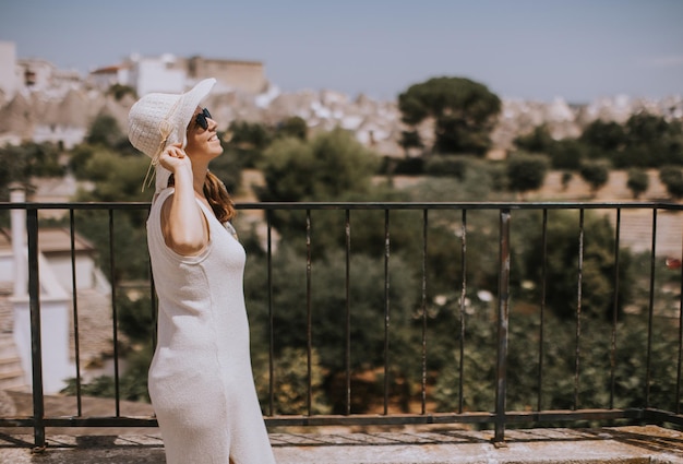 Una giovane donna in abito bianco e cappello in una giornata di sole durante la visita turistica ad Alberobello in Italia