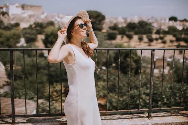 Una giovane donna in abito bianco e cappello in una giornata di sole durante la visita turistica ad Alberobello Italia