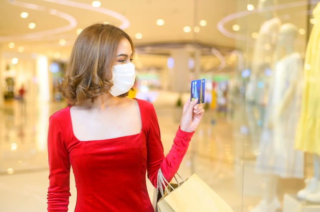 Una giovane donna in abito rosso che indossa una maschera protettiva nel centro commerciale