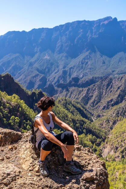 Una giovane donna in appoggio dopo il trekking sulla sommità di La Cumbrecita seduto nel punto di vista naturale guardando le montagne della Caldera de Taburiente, isola di La Palma, Isole Canarie, Spagna