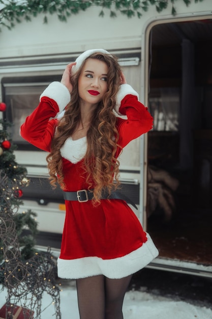 Una giovane donna in costume da Babbo Natale decora l'albero di Natale al campeggio invernale preparandosi per il