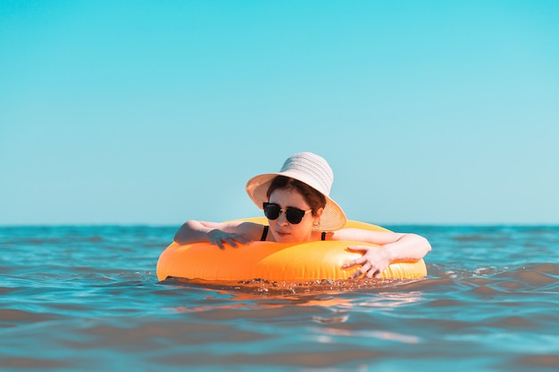 Una giovane donna in costume da bagno nero e cappello impara a nuotare con un cerchio.