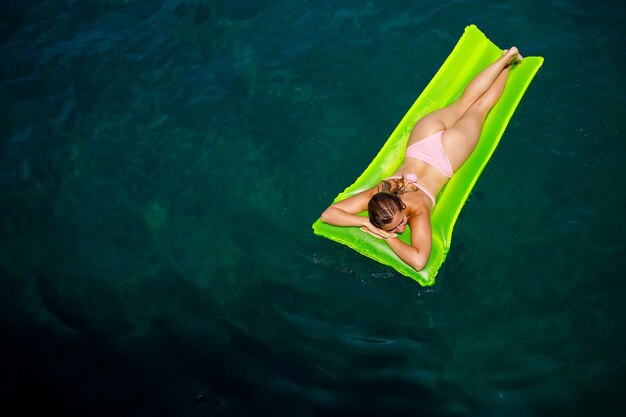 Una giovane donna in costume da bagno nuota su un materasso gonfiabile luminoso in mare. Concetto di vacanza estiva.