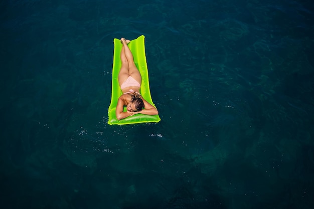 Una giovane donna in costume da bagno nuota su un materasso gonfiabile luminoso nel mare Concetto di vacanza estiva