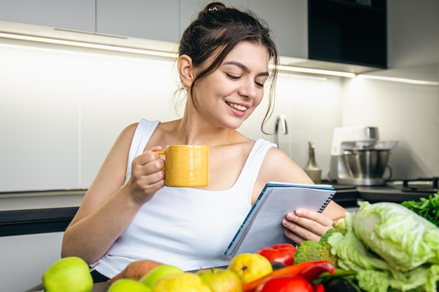 Una giovane donna in cucina con un taccuino in mano sceglie una ricetta