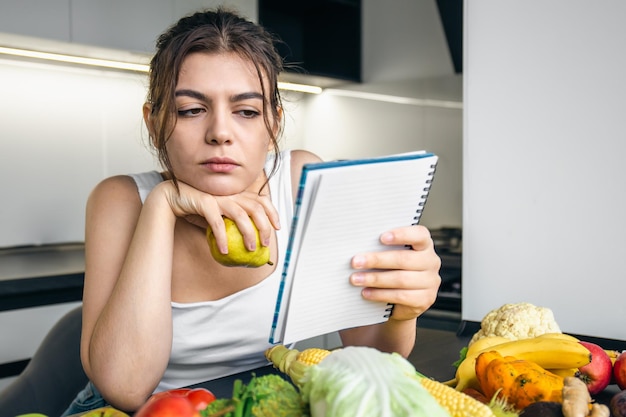 Una giovane donna in cucina con un taccuino tra le verdure