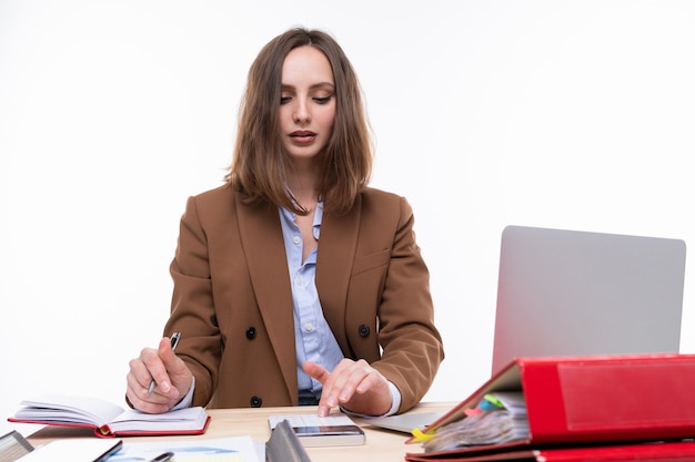 Una giovane donna in giacca e cravatta marrone conta su una calcolatrice sul posto di lavoro