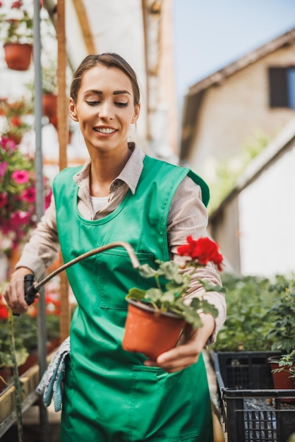 Una giovane donna in grembiule verde che innaffia i fiori in un centro di giardinaggio o in un vivaio.