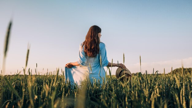 Una giovane donna in piedi in un campo di grano al tramonto.
