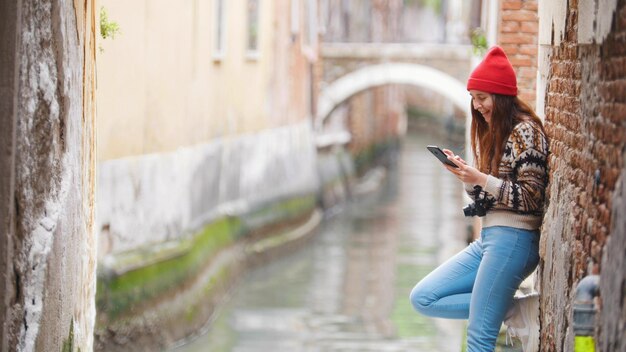 Una giovane donna in piedi vicino al canale dell'acqua e guardando nel suo telefono Venezia Italia