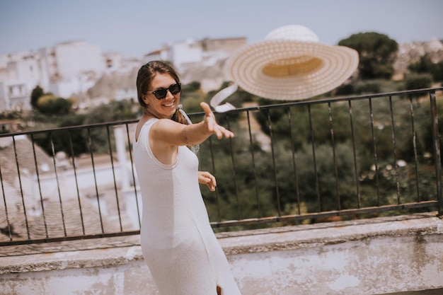 Una giovane donna in un abito bianco getta un cappello in una giornata di sole durante una visita turistica ad Alborebello Italia