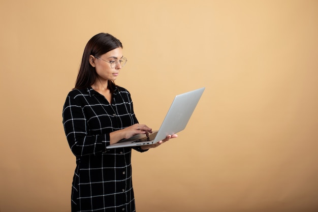 Una giovane donna in un abito scozzese si erge su uno sfondo arancione con un computer portatile