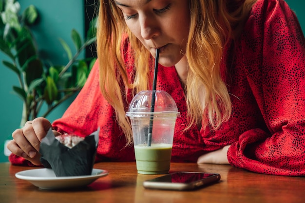 Una giovane donna in un caffè beve una bevanda verde latte ghiacciato