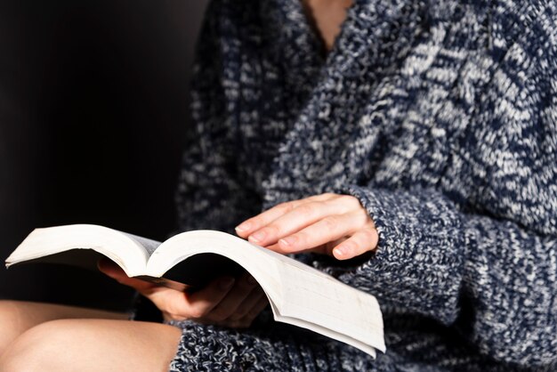 Una giovane donna in un maglione lavorato a maglia grigio sta leggendo un libro