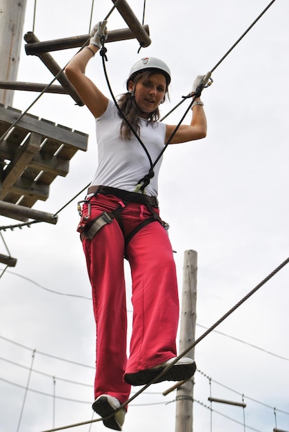 Una giovane donna in un parco divertimenti di corda cammina sul filo del rasoio con un'imbracatura di sicurezza e un casco