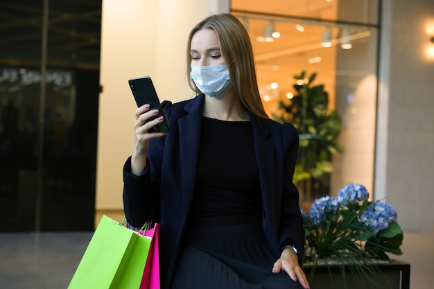 Una giovane donna in una maschera protettiva digita sul suo telefono dopo lo shopping