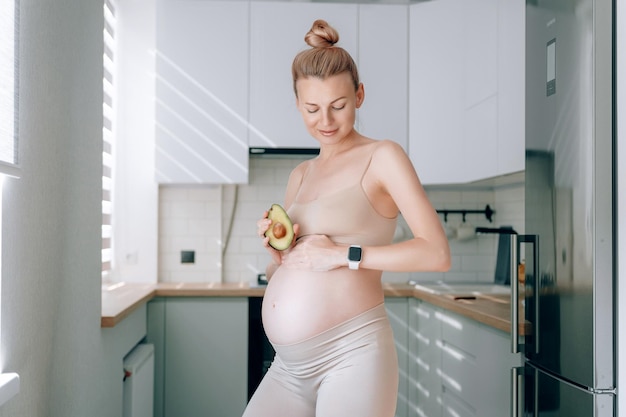Una giovane donna incinta di aspetto europeo nella sua cucina con un avocado tra le mani il concetto di una corretta alimentazione delle donne in gravidanza per il corretto sviluppo del feto