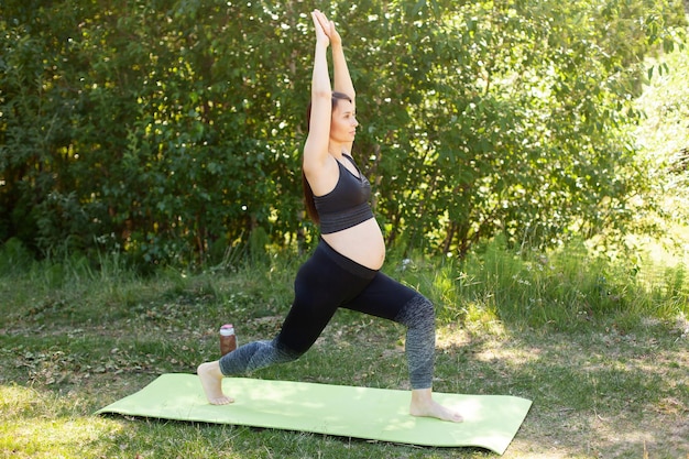 Una giovane donna incinta fa un tratto dopo l'allenamento in natura Sport per donne in gravidanza yoga salute verdi