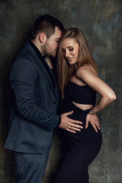 Una giovane donna incinta in un abito è in piedi su uno sfondo marrone. Foto scattata in uno studio fotografico