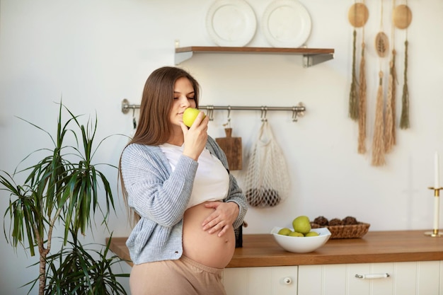 Una giovane donna incinta mangia una mela verde e ne gode il sapore