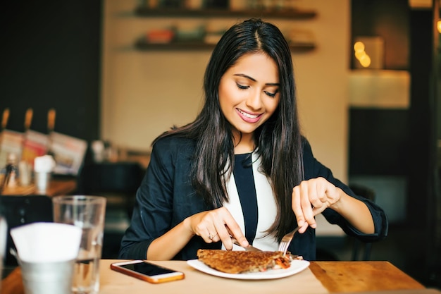 Una giovane donna indiana felice che mangia in un ristorante