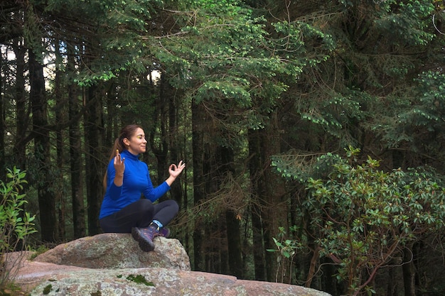 Una giovane donna ispanica a praticare yoga su una scogliera in una foresta