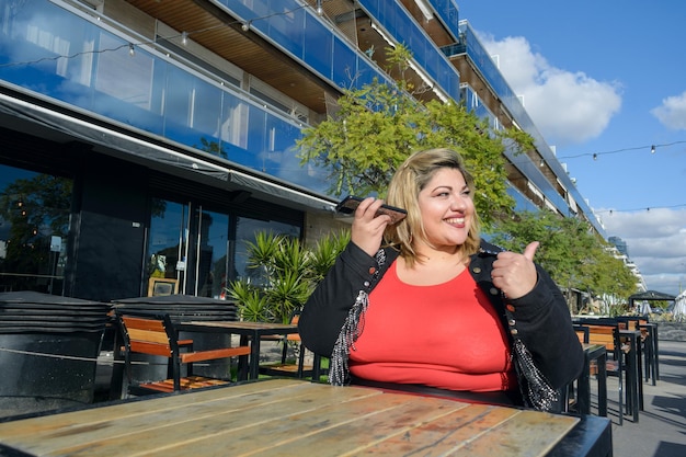 Una giovane donna latina seduta fuori dal ristorante che ascolta un messaggio vocale sul suo telefono.