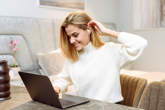 Una giovane donna lavora con un laptop nel suo appartamento. Imprenditrice freelance in cuffia tiene una riunione di lavoro da casa.