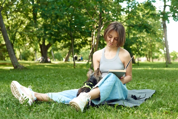 Una giovane donna legge un libro nella natura accanto al suo piccolo cane Yorshir Terrier