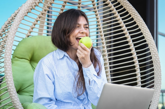 Una giovane donna mangia una mela e lavora su un laptop